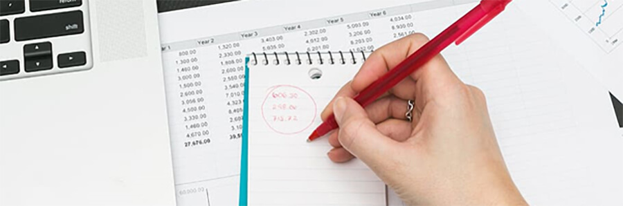 Woman's hand writing figures in a notepad with a red pen.