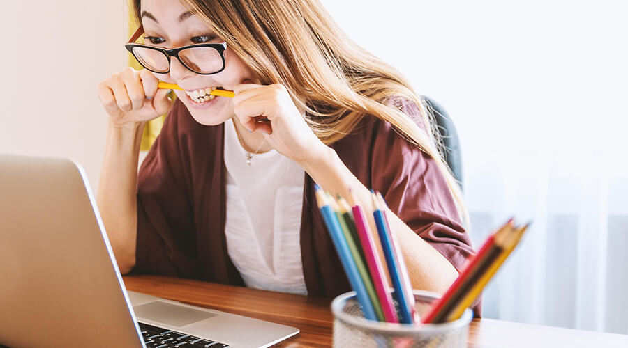 Woman looking at a laptop while biting her pencil.