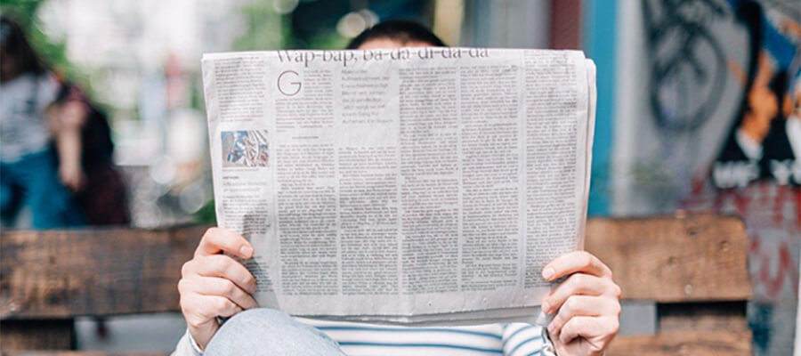 Person reading a newspaper on a park bench.