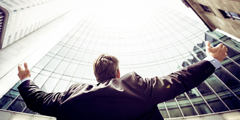 Businessman looking up at a skyscraper with his arms open wide.