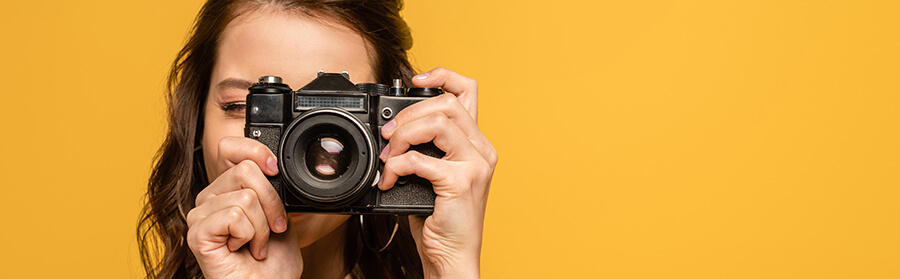 Woman holding a camera on a yellow background.