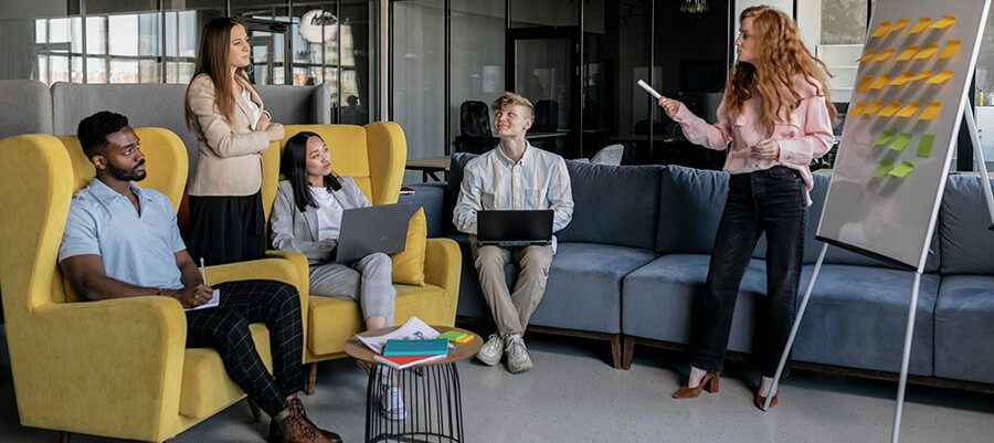 Five people attending a relaxed business meeting on sofas with a whiteboard.