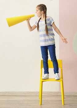 Child standing on a chair talking into a megaphone.