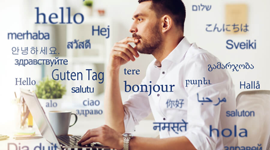 Man looking at laptop with 'hello' in many different langauges.