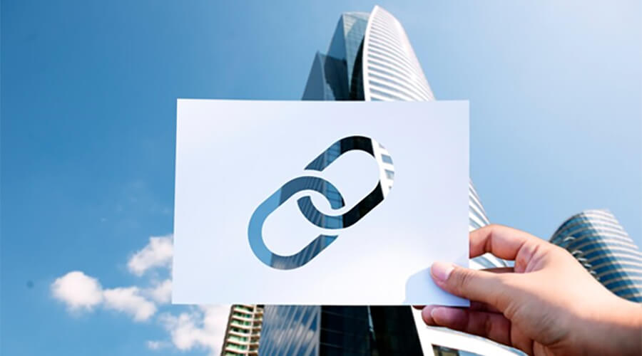 Person holding a piece of paper with a hole in the shape of a link in front of a skyscraper.