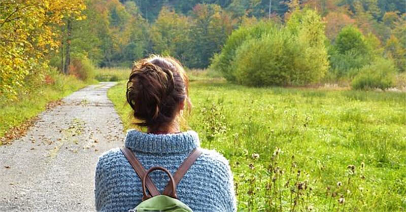 A girl in a sweater setting out on a journey down a country road, representing the idea to move away and start over.