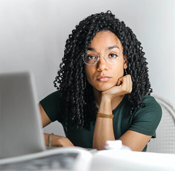 Female student with glasses gazes beyond her laptop.