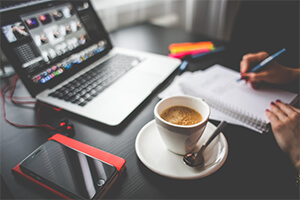 Busy freelancer with laptop, phone and coffee writing in a notepad.