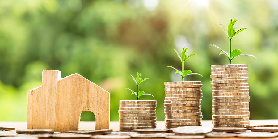 Piles of coins with saplings growing out of them with a wooden model of a house.