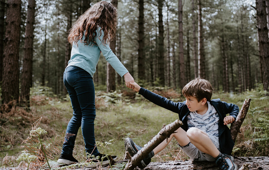 Girl helping a boy up after a fall in a forest.