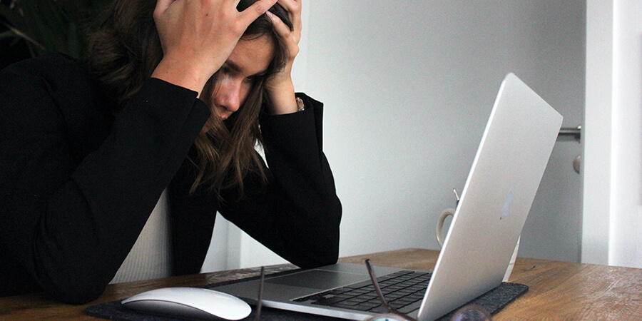 Stressed person holding their head and leaning over a laptop.