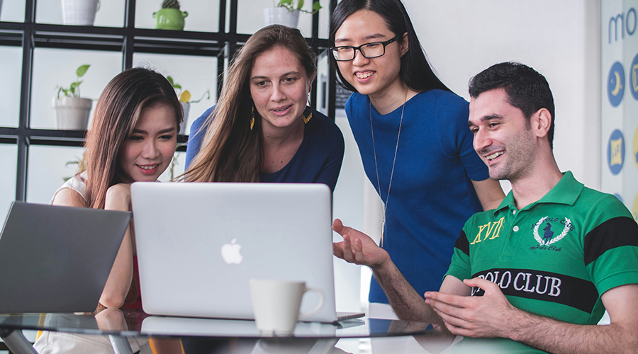 Four young professionals looking at a laptop screen.